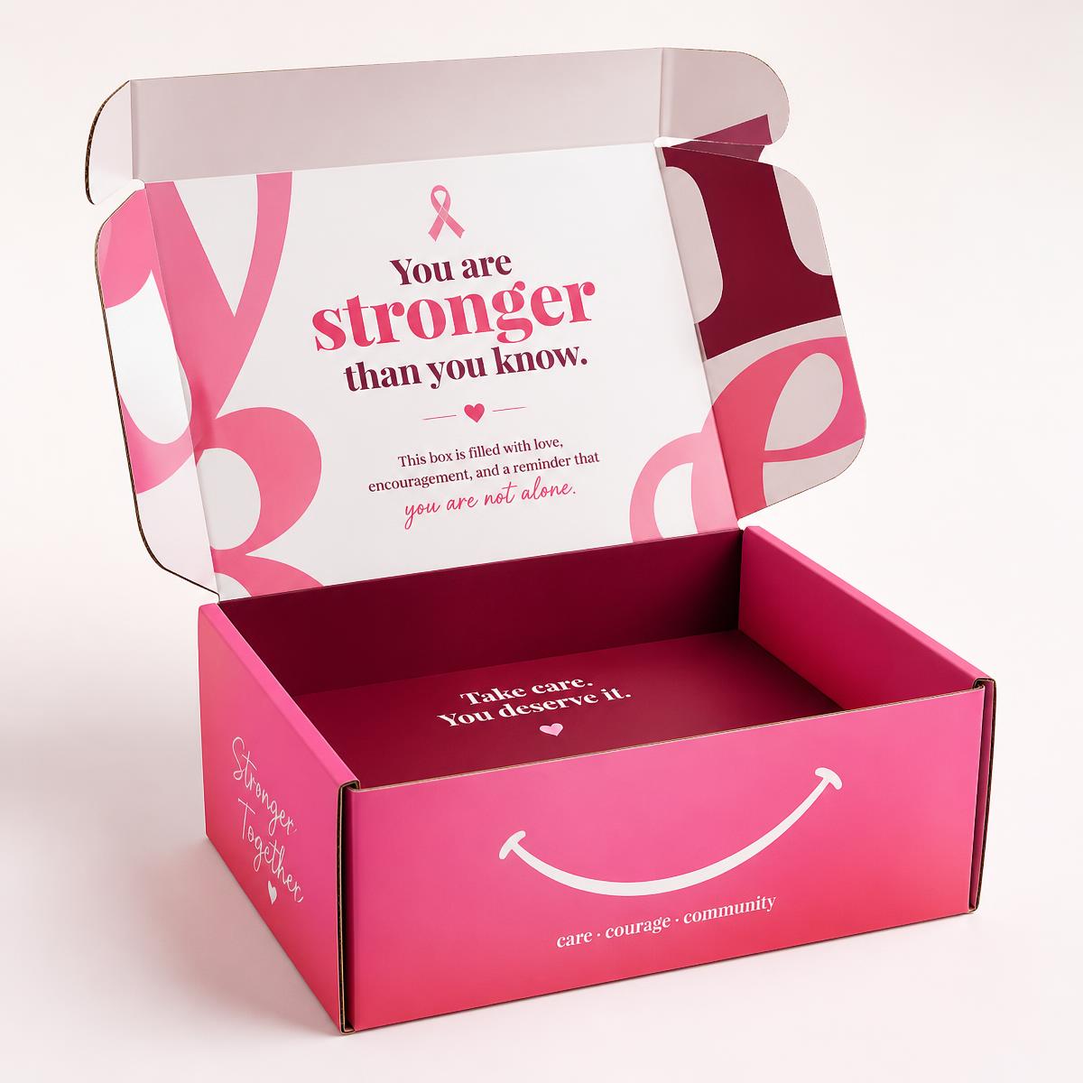 An open StrongHer Box care package with a soft pink ribbon, folded textiles, and skincare items